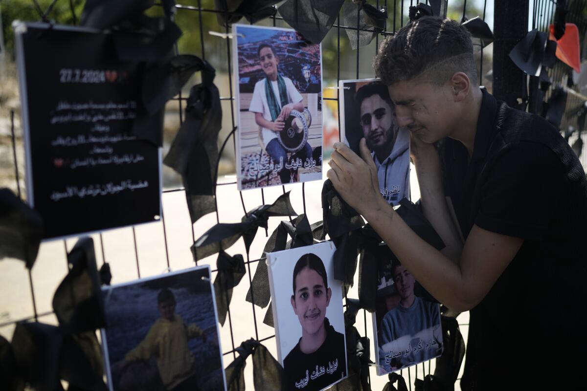 A young man weeps over a makeshift memorial of photos posted on a fence.