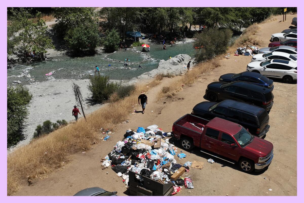 A pile of trash on a river bank next to a line of parked cars