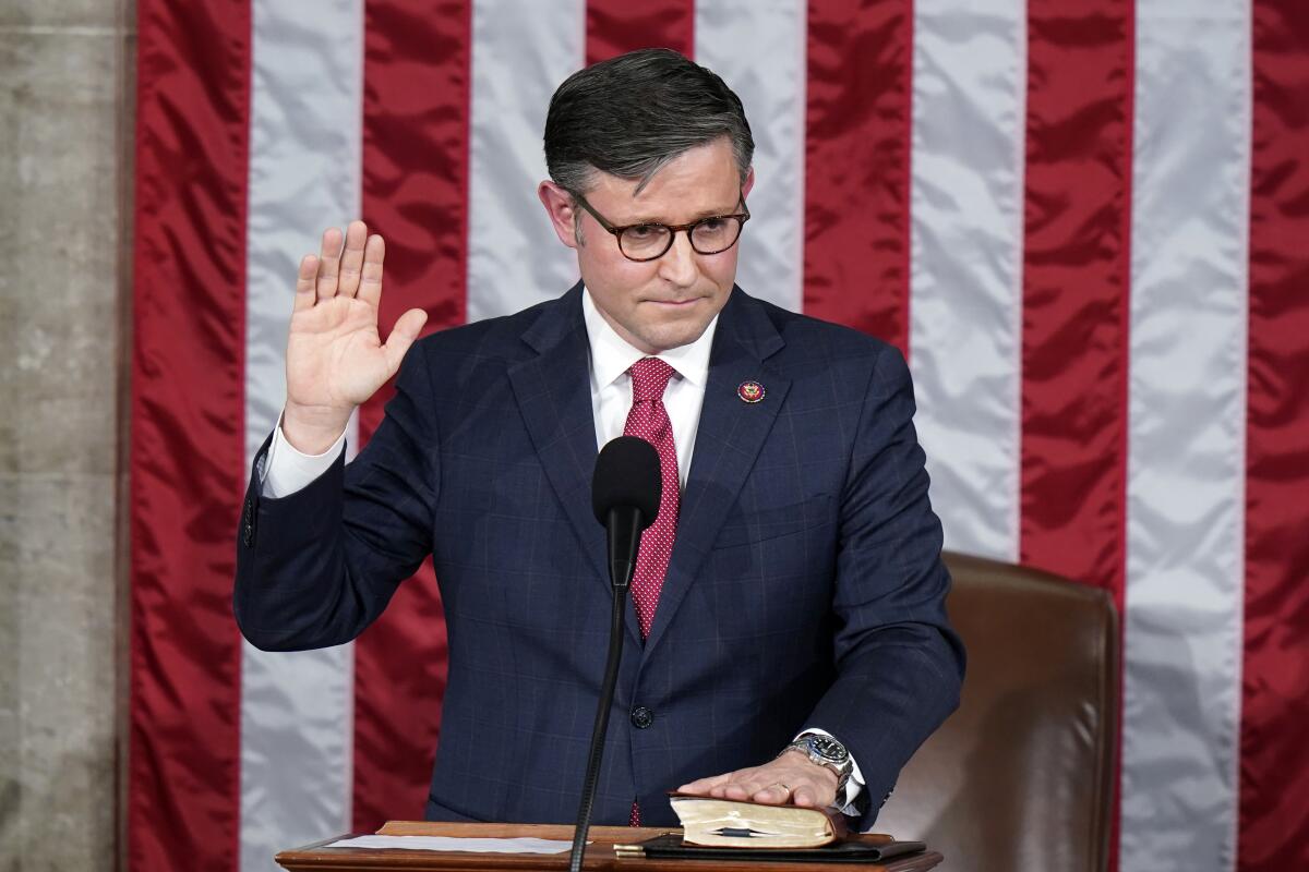 Rep. Mike Johnson (R-La.), wearing a dark suit and white shirt is seen raising his right hand to take the oath.