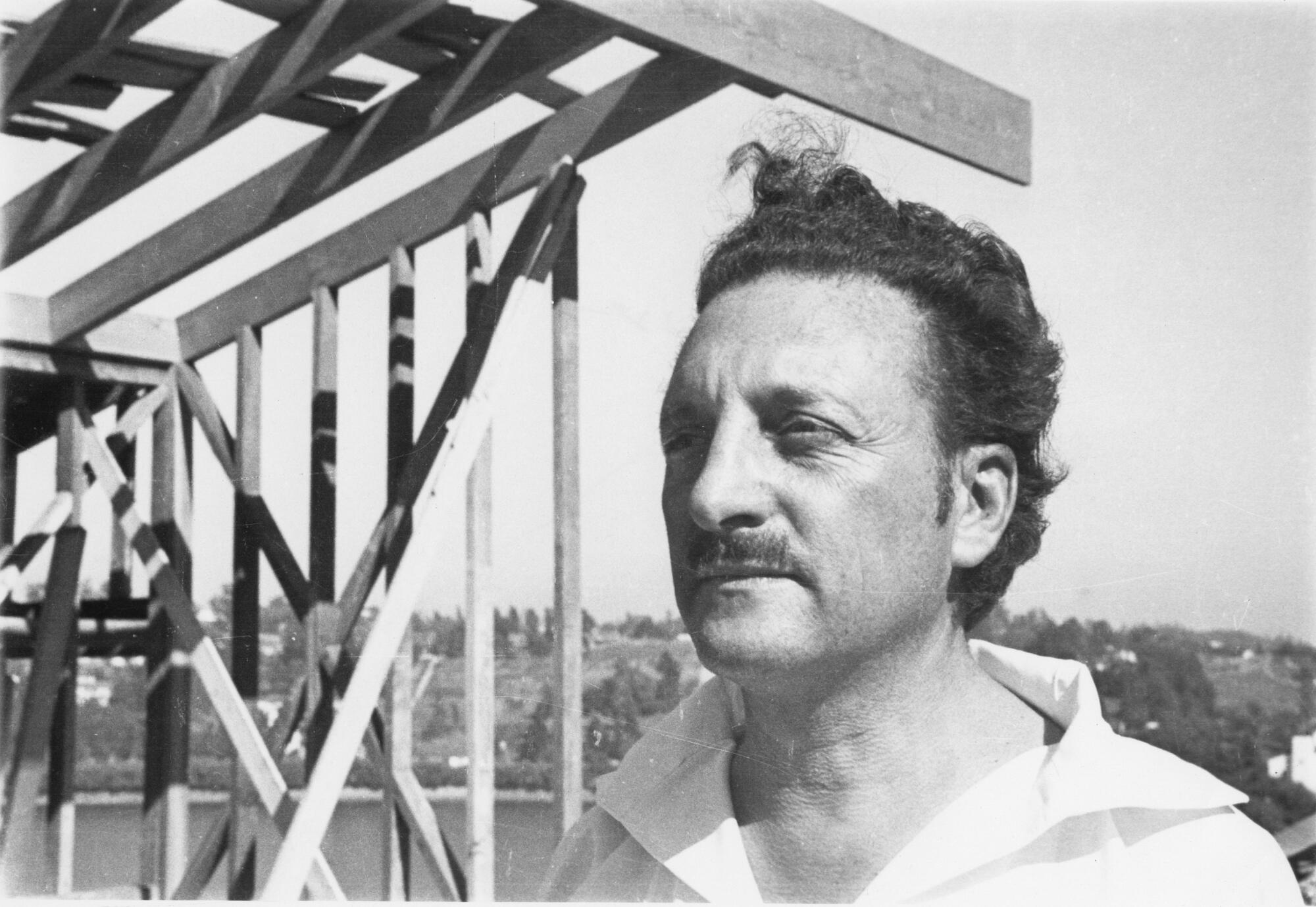 A man with a mustache stands at a construction site.