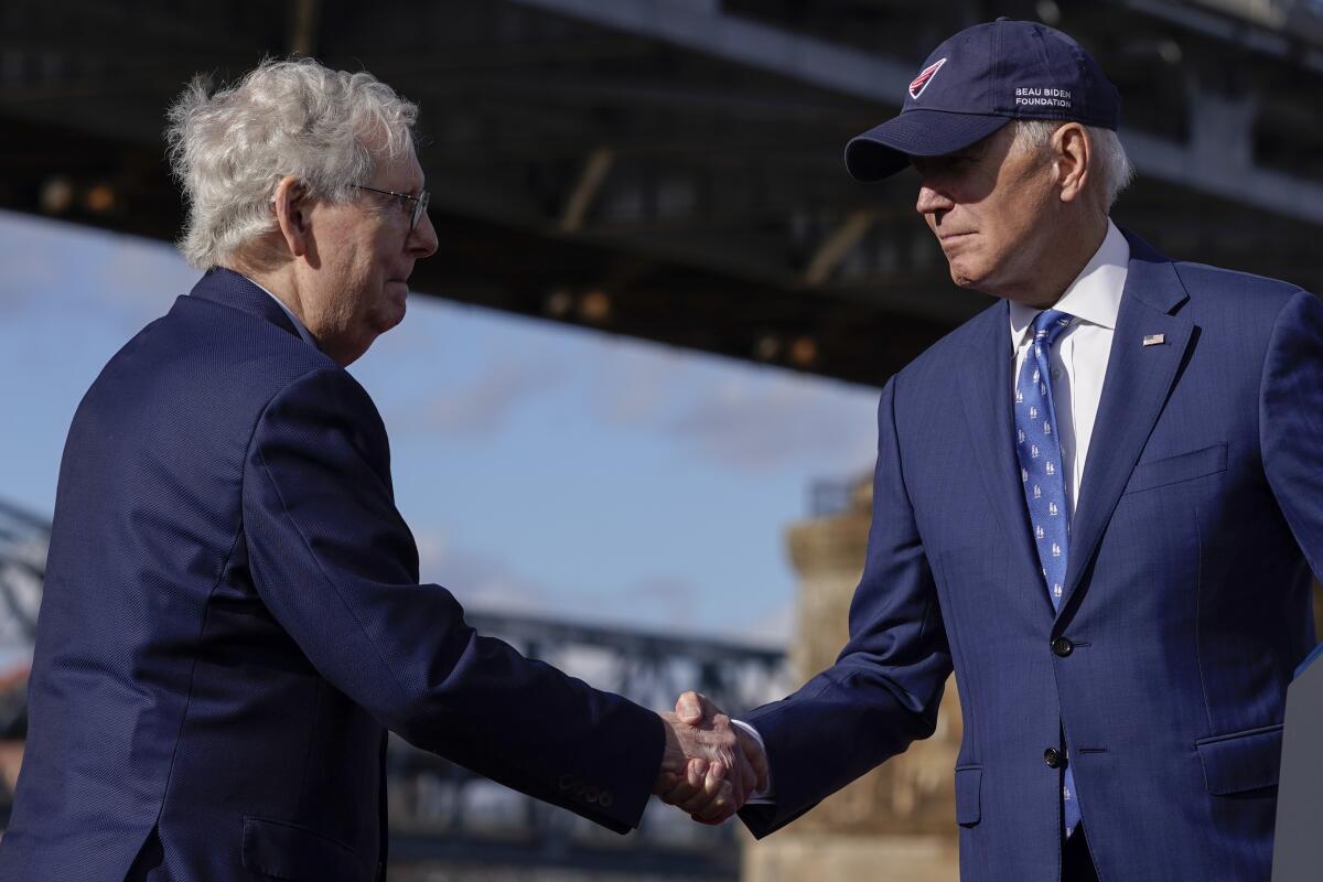 President Biden, in a baseball cap, shaking hands with Senate Minority Leader Mitch McConnell outdoors.