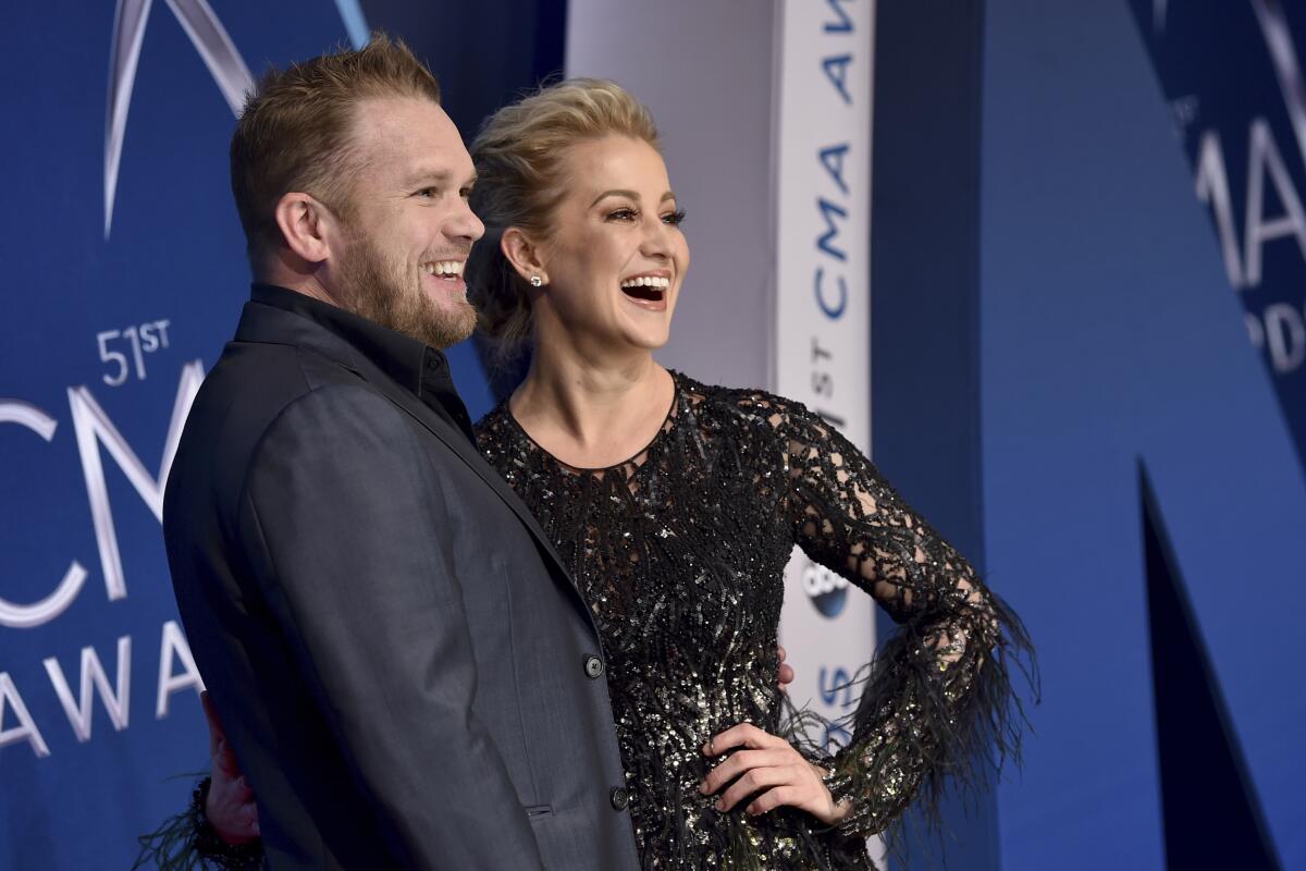 Kyle Jacobs and Kellie Pickler smile and pose together in formal attire against a blue backdrop.
