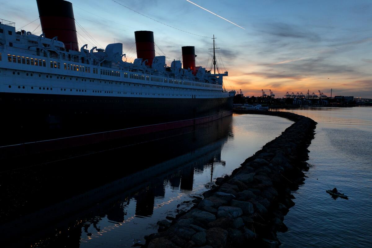 A person fishes from a kayak with a view of the historic RMS Queen Mary ocean liner.