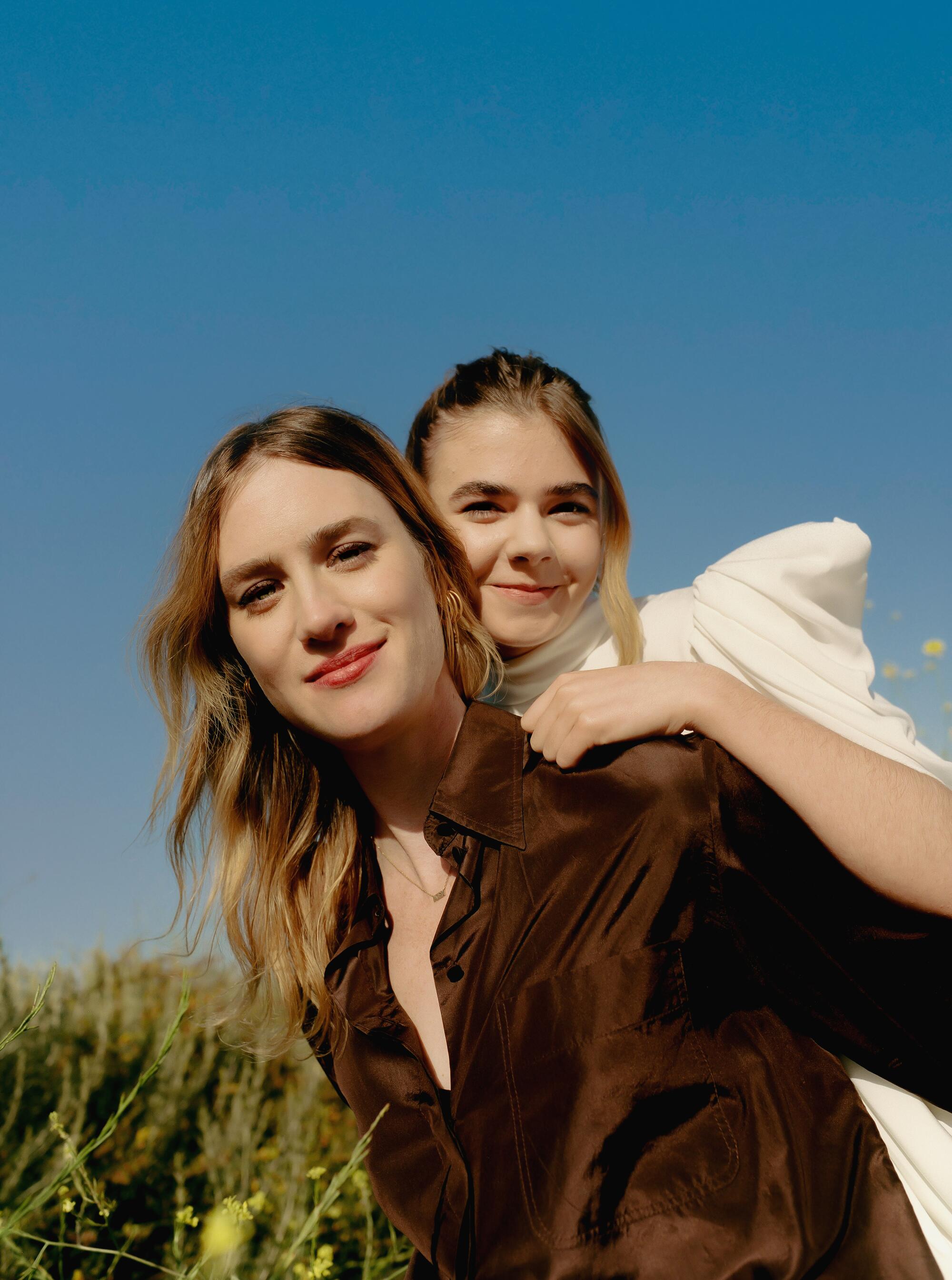 A woman gives a girl a piggyback ride amid yellow flowers in a field.