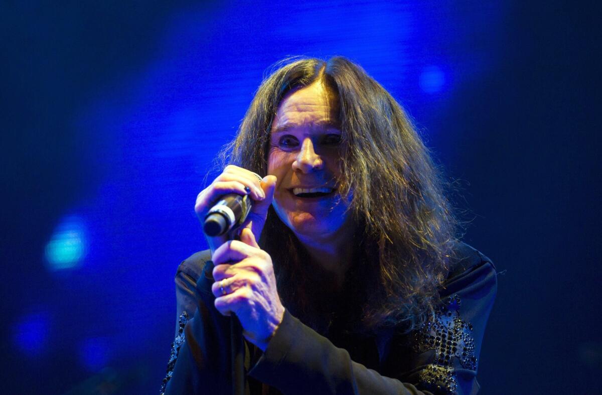 Ozzy Osbourne smiles as he holds a microphone.
