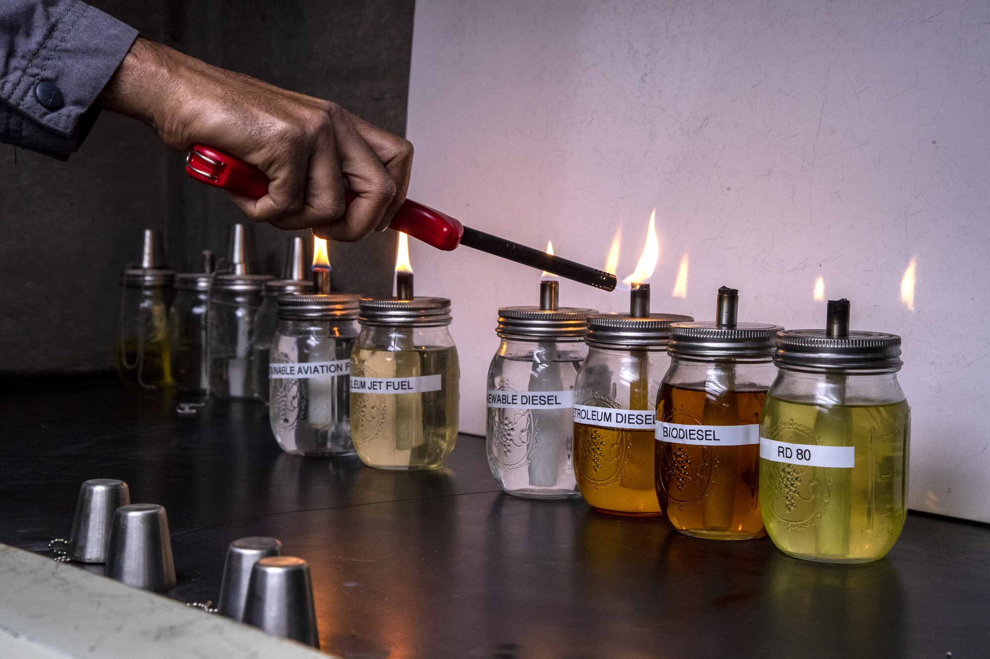 A man lights wicks atop a row of jars filled with various liquids