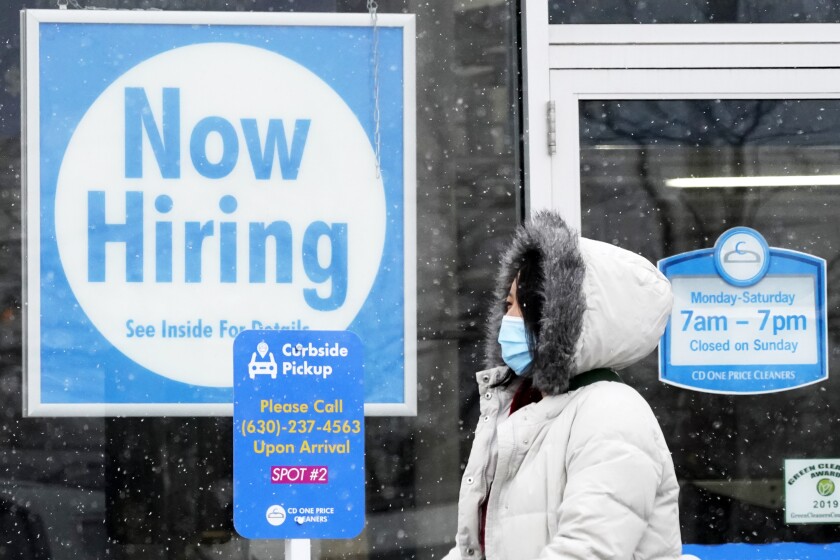 FILE - In this Feb. 6, 2021 file photo, a woman walks past a "Now Hiring" sign displayed at a CD One Price Cleaners in Schaumburg, Ill. In a stark sign of the economic inequality that has marked the pandemic recession and recovery, Americans as a whole are now earning the same amount of wages and salaries that they did before the pandemic struck, even with nearly 9 million fewer people at work. (AP Photo/Nam Y. Huh, File)