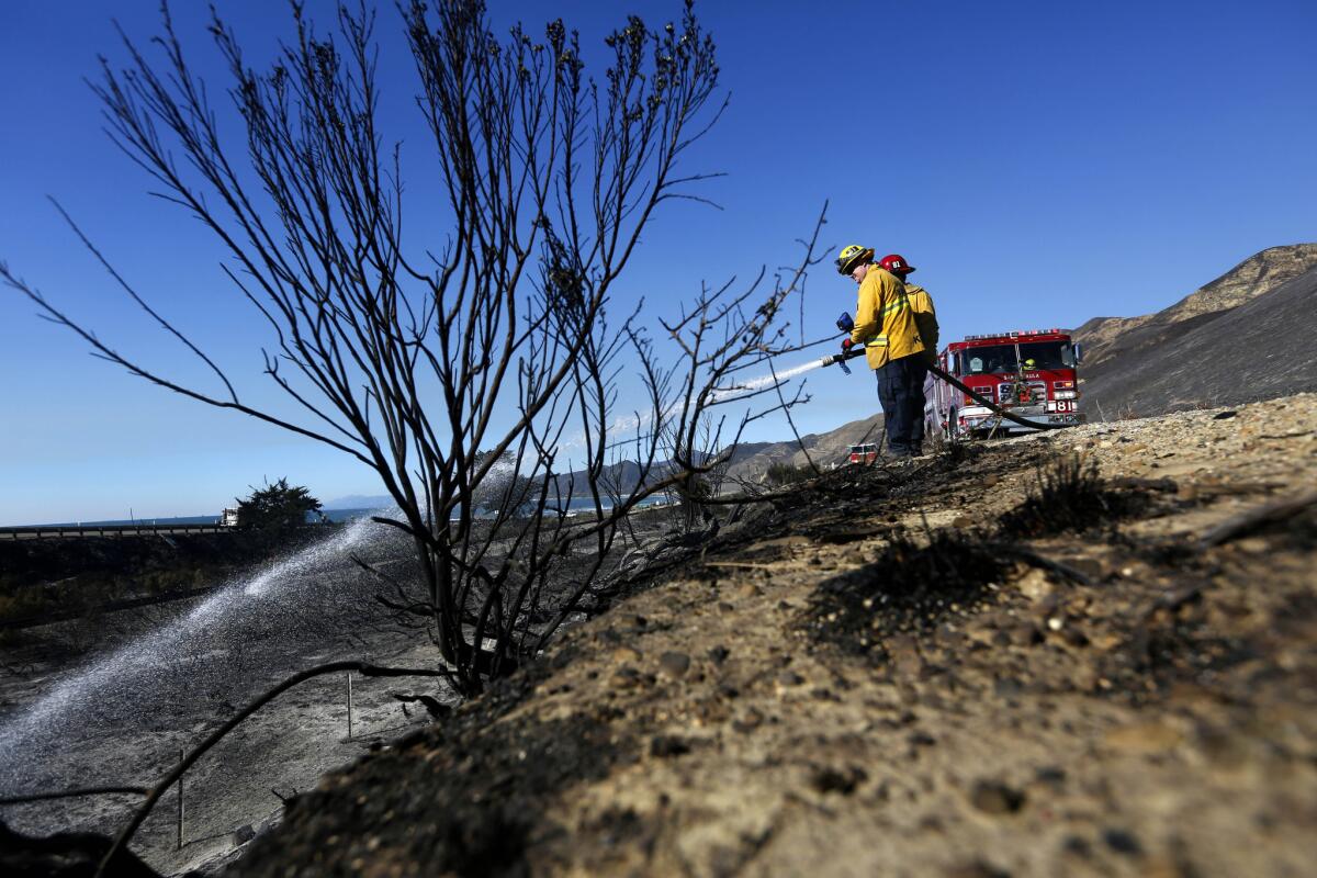 A 1,200-acre brush fire burned in the hills above Solimar Beach in Ventura County in the early morning hours Saturday. Mandatory evacuation orders were issued for residents along the coastal area, though those homes are no longer under threat. Firemen from Santa Paula Fire Department hose down hot spots along the 101 freeway, which had a 15-mile stretch shut down as a result of the blaze. (Michael Robinson Chavez / Los Angeles Times)