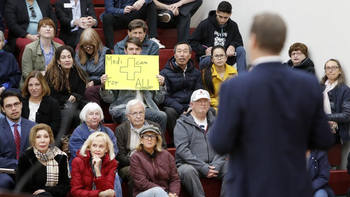 A constituent holds up a sign stating Medicare-for-all as Rep. Harley Rouda (D-Laguna Beach) addresses a question about Medicare during Rouda's first district town hall meeting in the gym at Estancia High School in Costa Mesa on Tuesday.