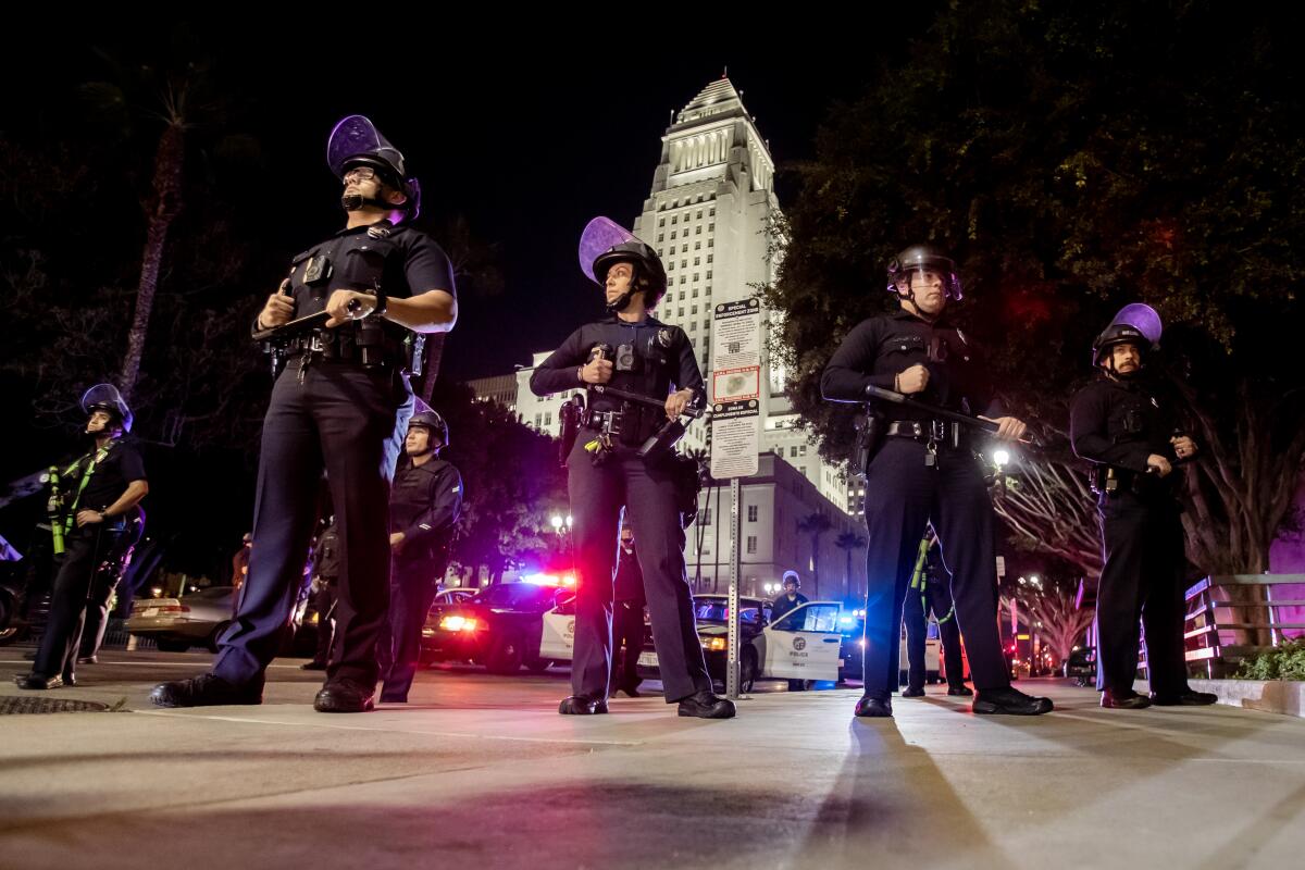 A line of police officers holding batons and wearing riot helmets in front of City Hall