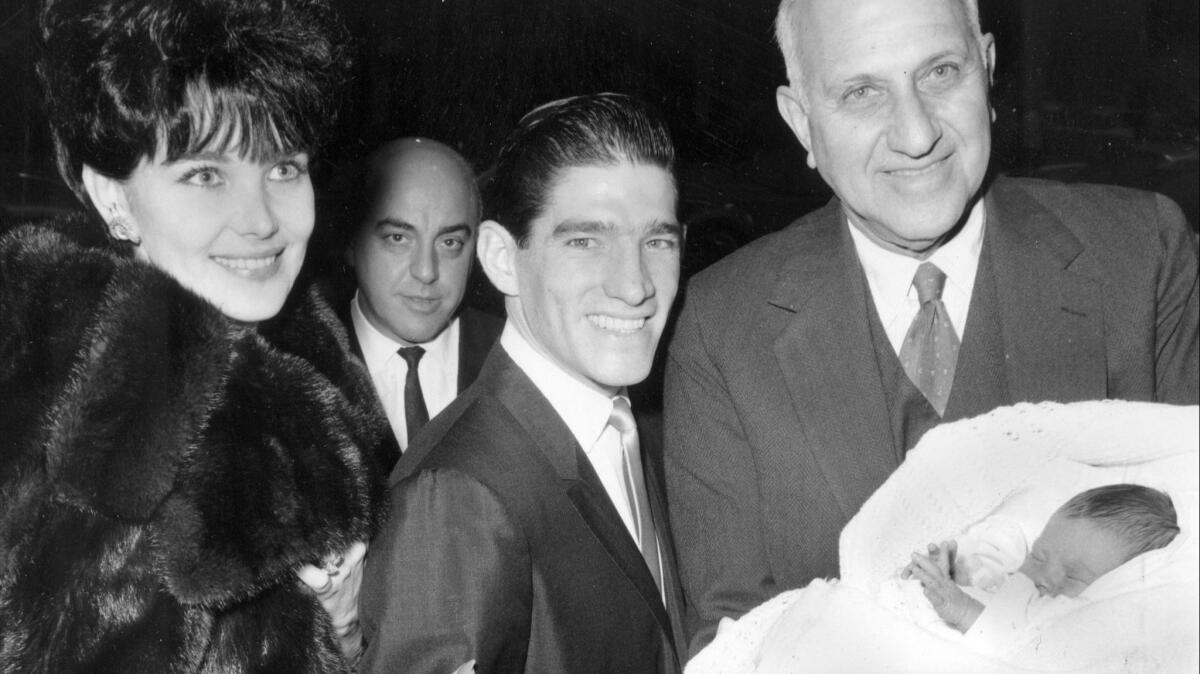 Harry F. Guggenheim, right, holds the newly christened firstborn child of jockey Manuel Ycaza and his then-wife, Linda, in 1963.