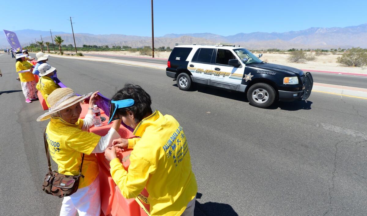 A police vehicle drives by as Falun Gong practitioners place banners on a barricade near where President Obama was meeting with Chinese President Xi Jinping in Rancho Mirage.