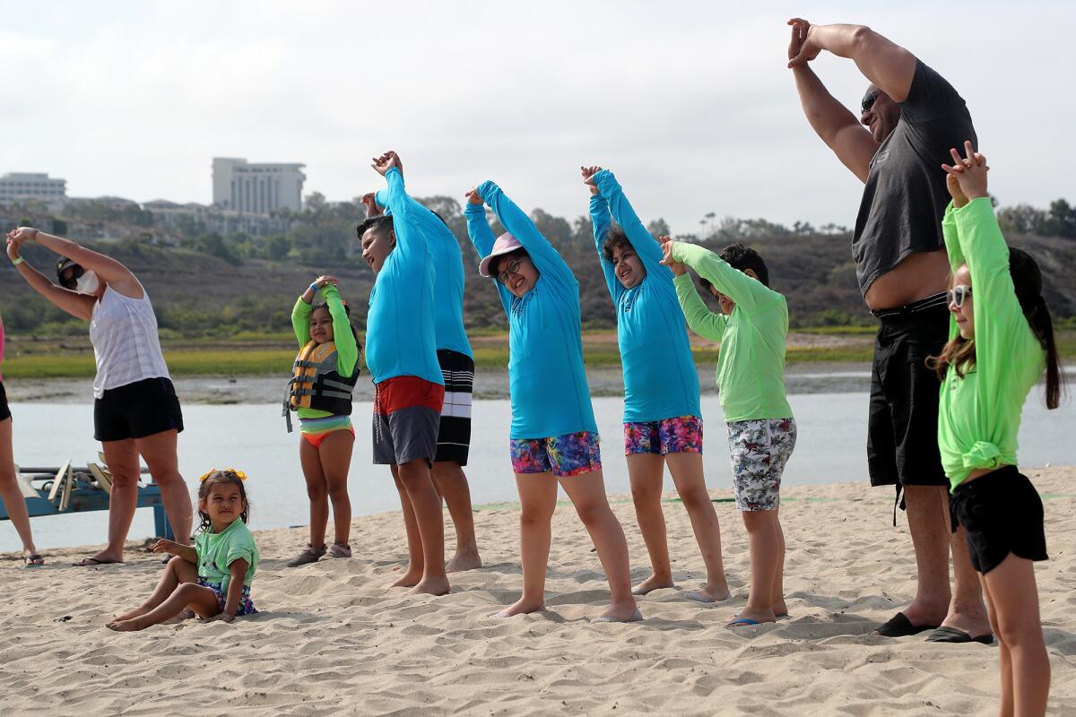 Children and parents stretch as they warm up before paddling out to Newport Dunes on Thursday.