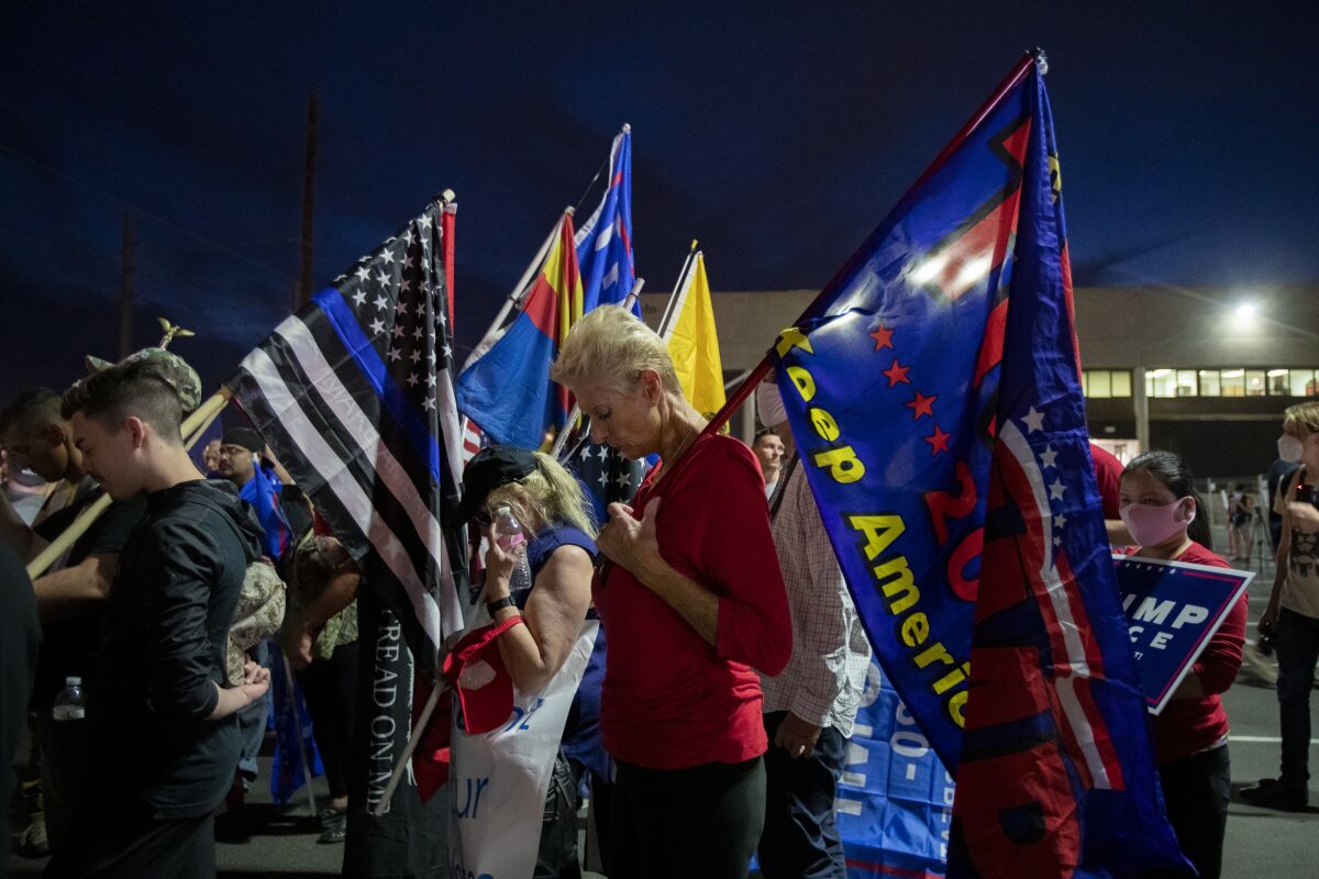Trump supporters bow their heads in prayer while protesting in the parking lot at the Maricopa County