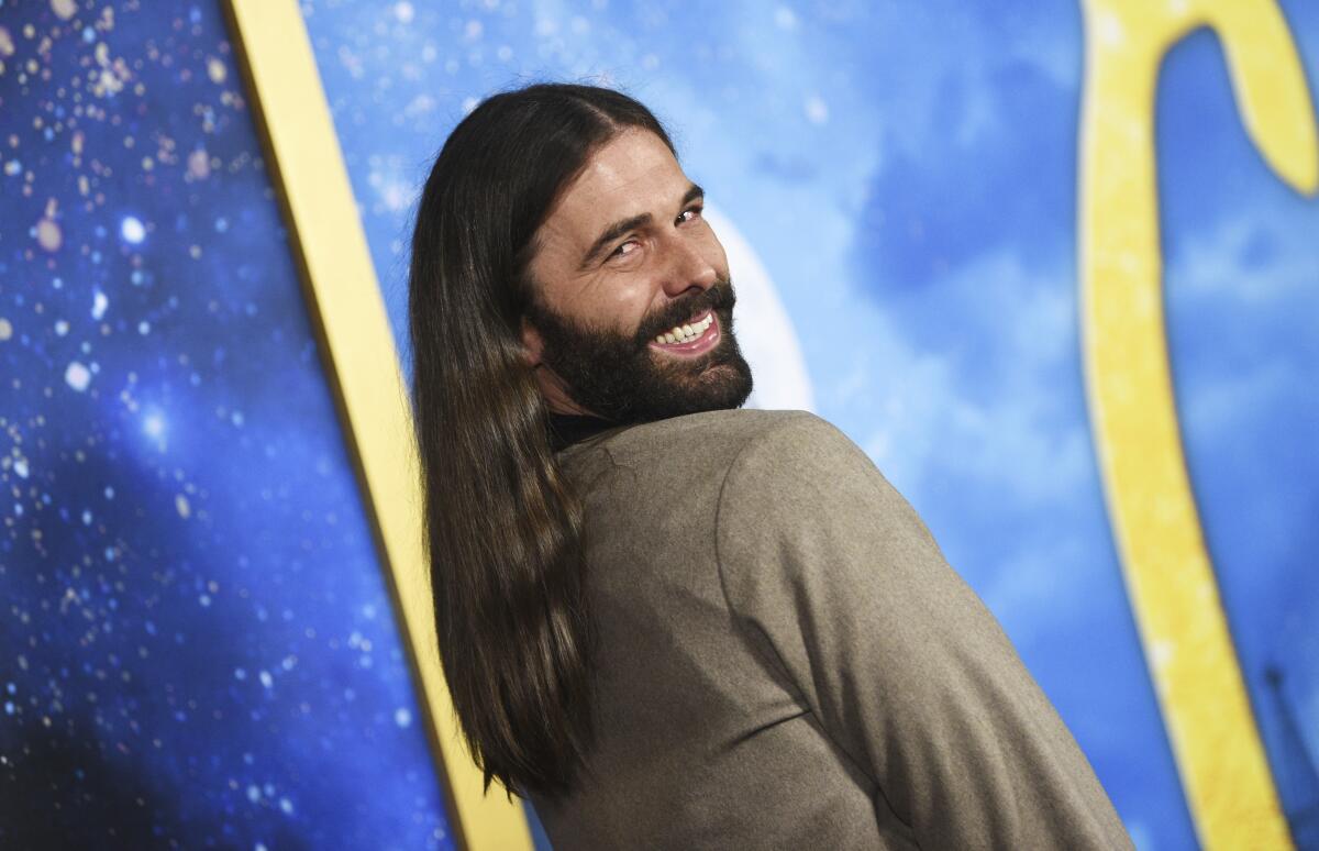 Jonathan Van Ness looks over his shoulder and smiles while wearing a brown jacket