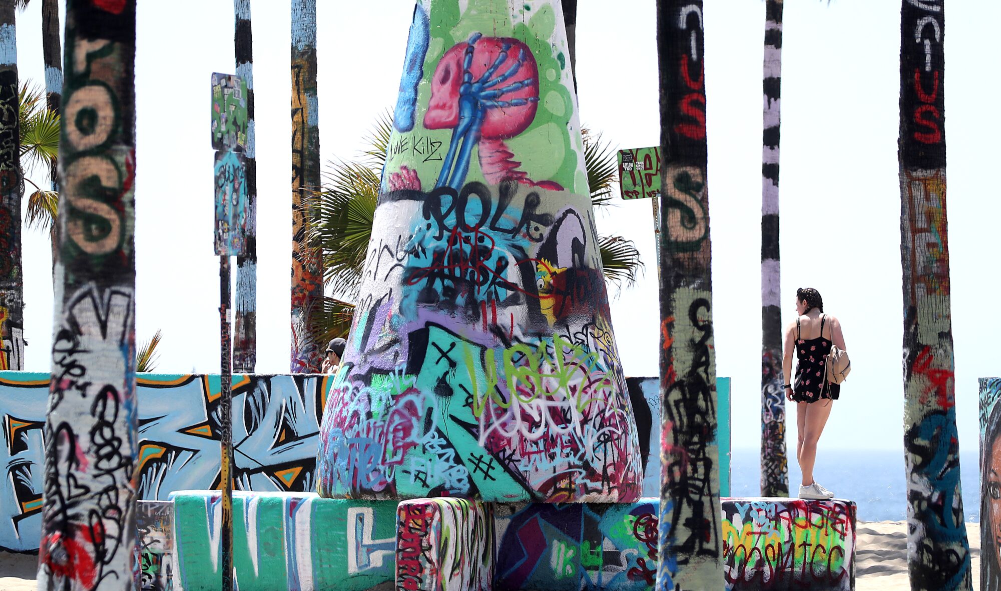 A beachgoer stands among graffiti on walls and trees at the beach