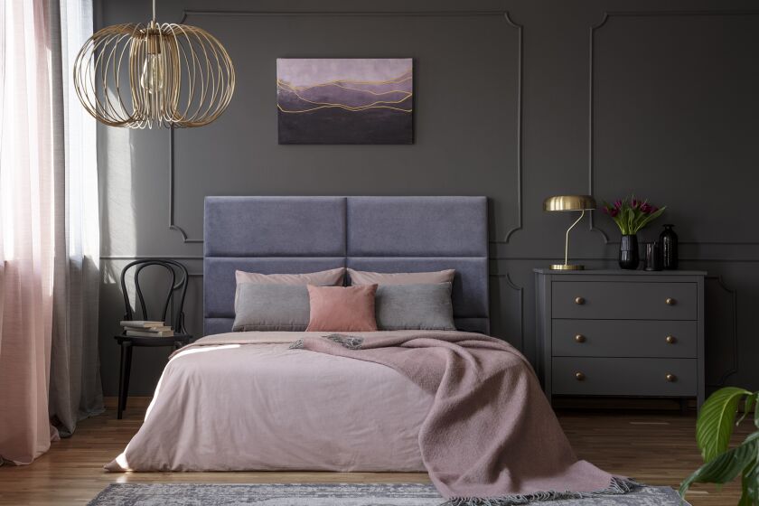 An elegant bedroom with a custom upholstered headboard, muted but statement-making color on wall, nontraditional nightstands.