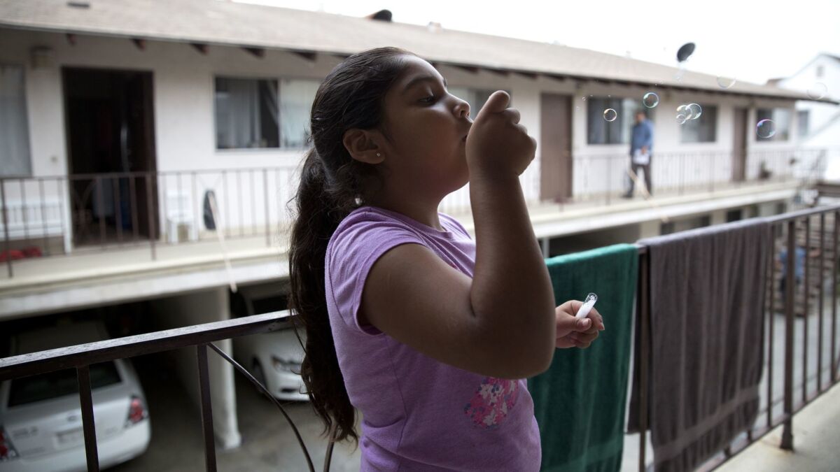 As her family packs the car to move, Luz Madrigal, 6, blows bubbles on the balcony of her apartment in Gardena. (Brian van der Brug / Los Angeles TImes)