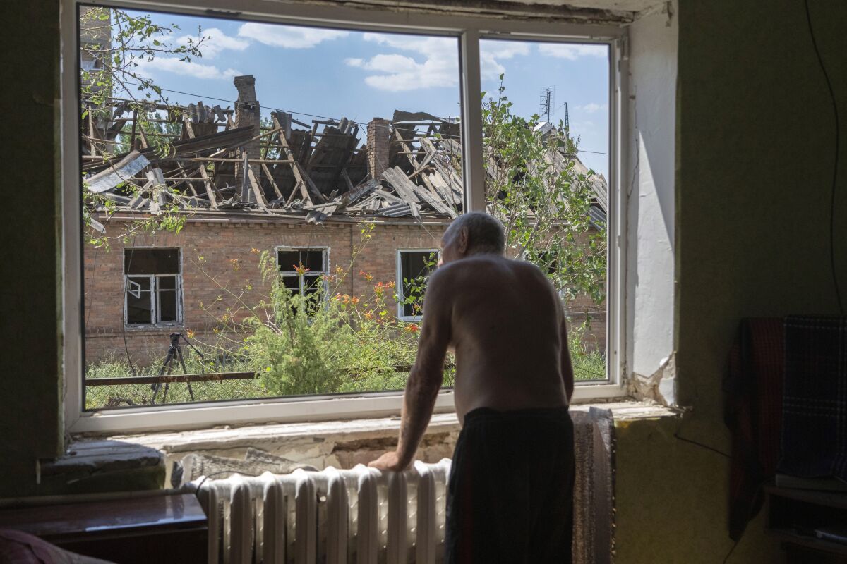 A man looks out of a broken window of a damaged  house.