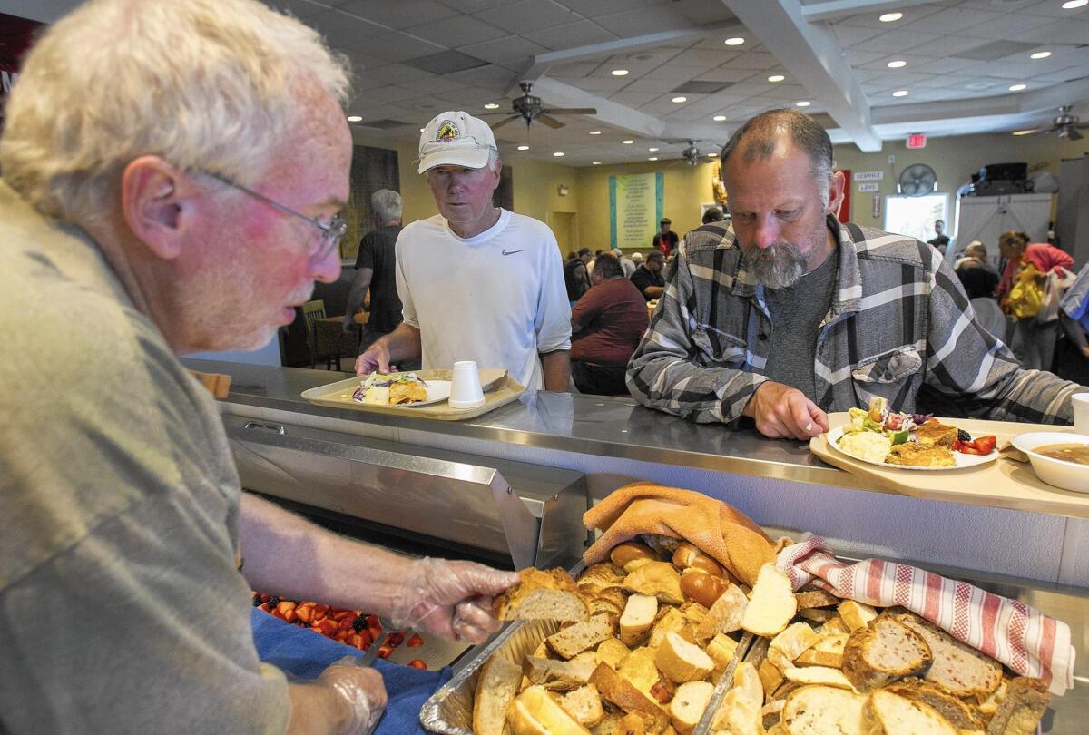 Al Nieman, left, serves food to Dennis Sundman, center, and Shannon Carder at the Someone Cares Soup Kitchen in Costa Mesa in March 2015.