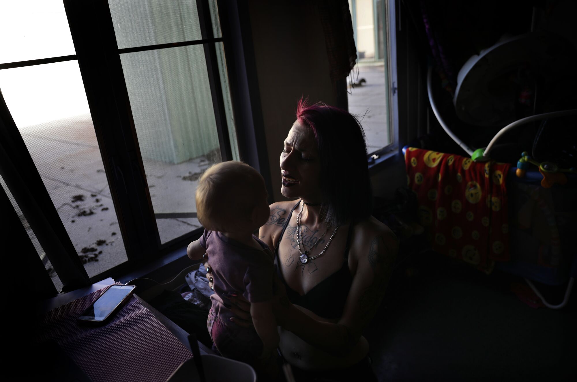 A woman singing to a baby in a darkened room lit by windows behind them.