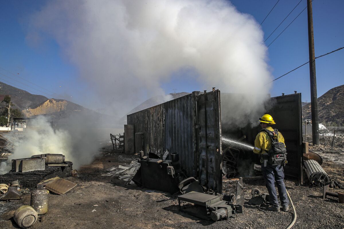 A firefighter hoses down the smoking hulk of a shipping container