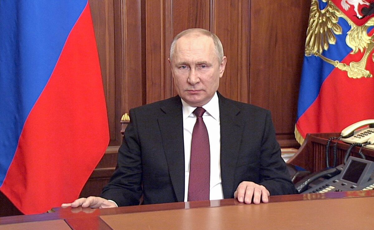 Russian President Vladimir Putin appearing stern as he sits at a desk flanked by flags