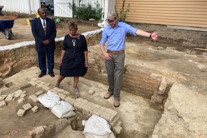 Reginald F. Davis, from left, pastor of First Baptist Church in Williamsburg, Connie Matthews Harshaw, a member of First Baptist, and Jack Gary, Colonial Williamsburg's director of archaeology, stand at the brick-and-mortar foundation of one the oldest Black churches in the U.S. on Wednesday, Oct. 6, 2021, in Williamsburg, Va. Colonial Williamsburg announced Thursday Oct. 7, that the foundation had been unearthed by archeologists. (AP Photo/Ben Finley)
