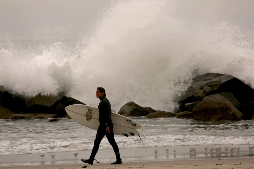 A surfer walks past the breakwater in Venice as tsunami warnings did not keep surfers away.