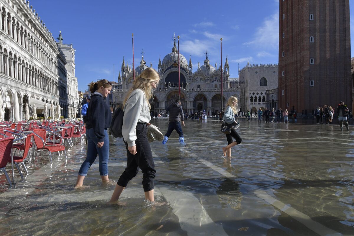 People walk in a flooded St. Mark's Square in Venice, Italy, Friday, Nov. 5, 2021. After Venice suffered the second-worst flood in its history in November 2019, it was inundated with four more exceptional tides within six weeks, shocking Venetians and triggering fears about the worsening impact of climate change. (AP Photo/Luigi Costantini)