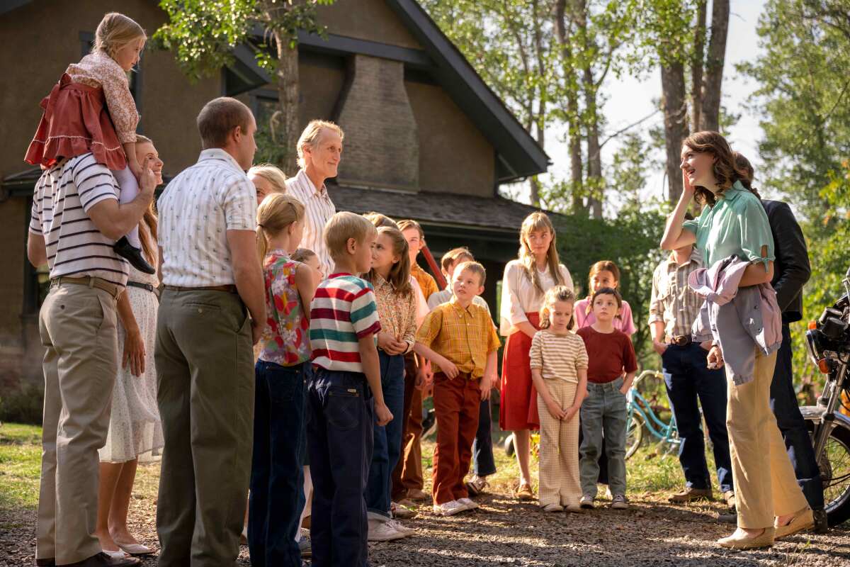 A young woman is greeted by a large, multigenerational family standing in front of their house 