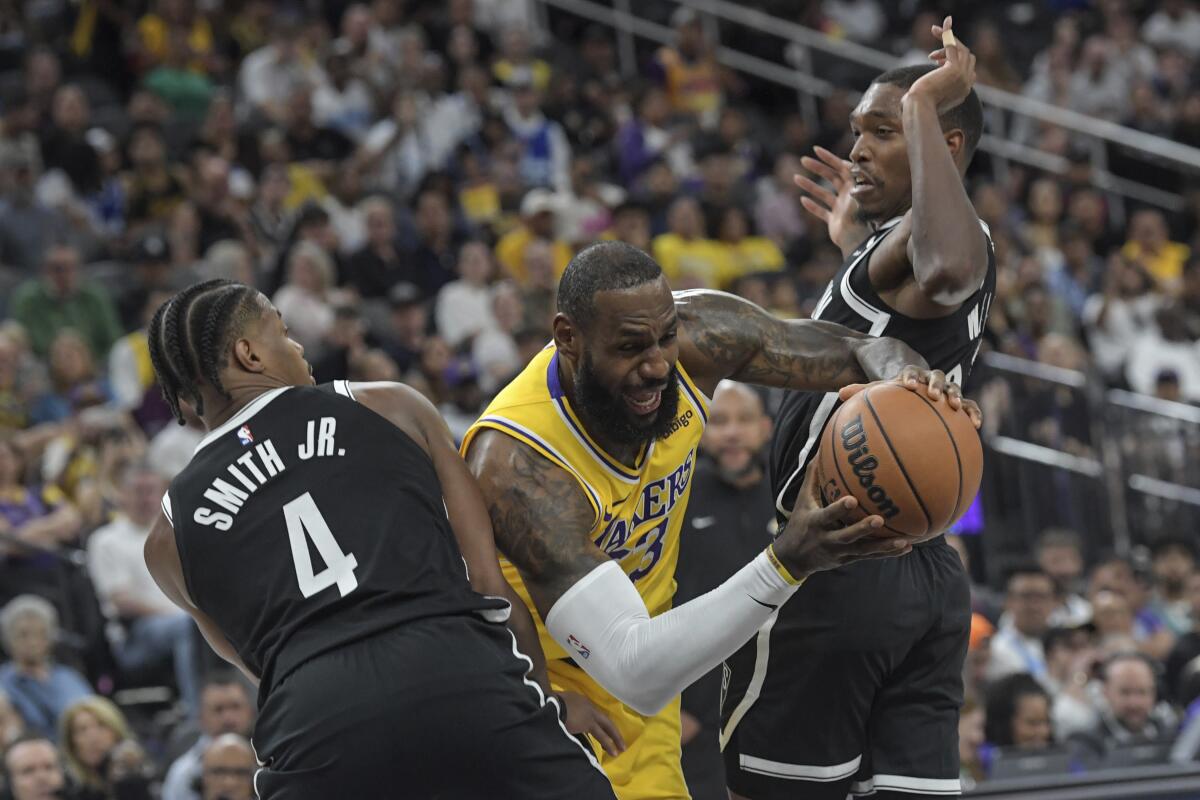 Lakers forward LeBron James tries to power his way between Nets guards Dennis Smith Jr., left, and Lonnie Walker IV.