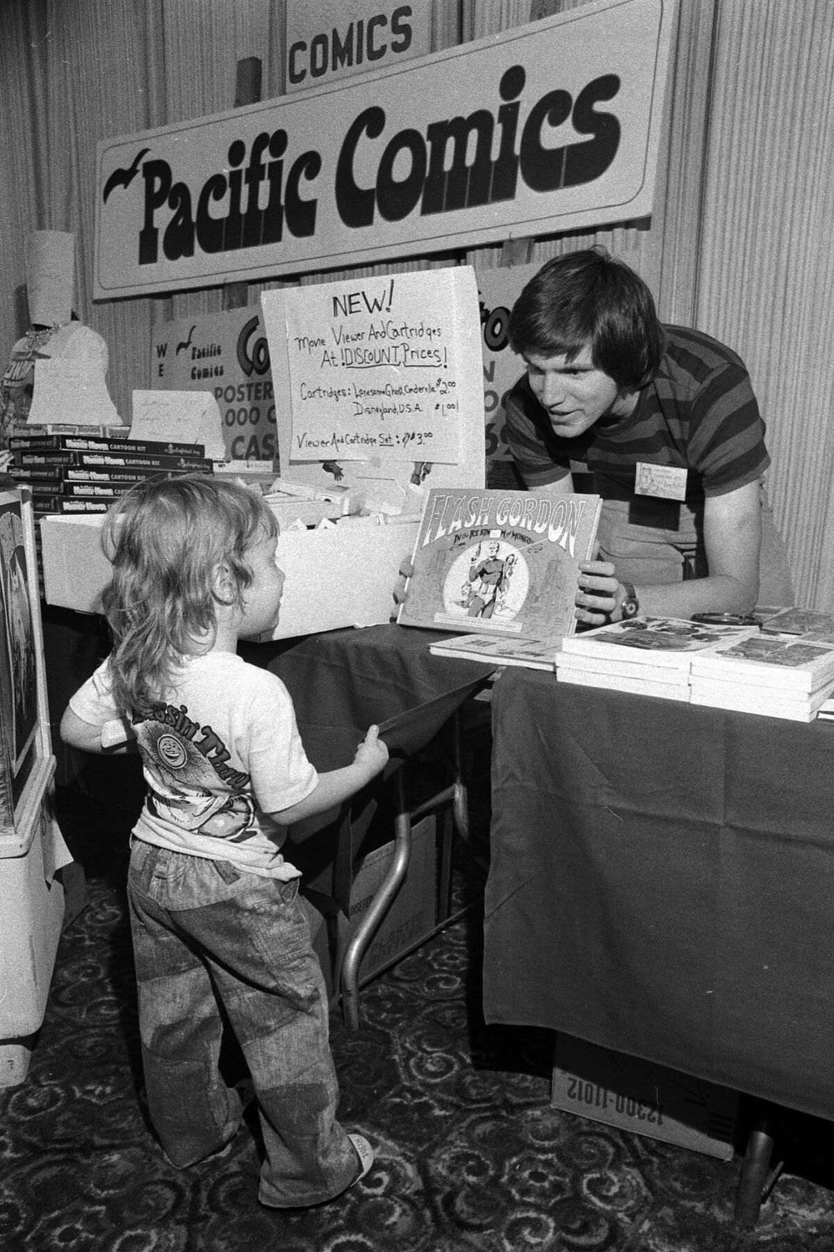 Bill Lund shows a Flash Gordon book to little Harry Knowles, 3-1/2, of Austin, Texas, at the San Diego Comic-Con in the El Cortez Hotel. Knowles would go on to found the website Ain't It Cool News.