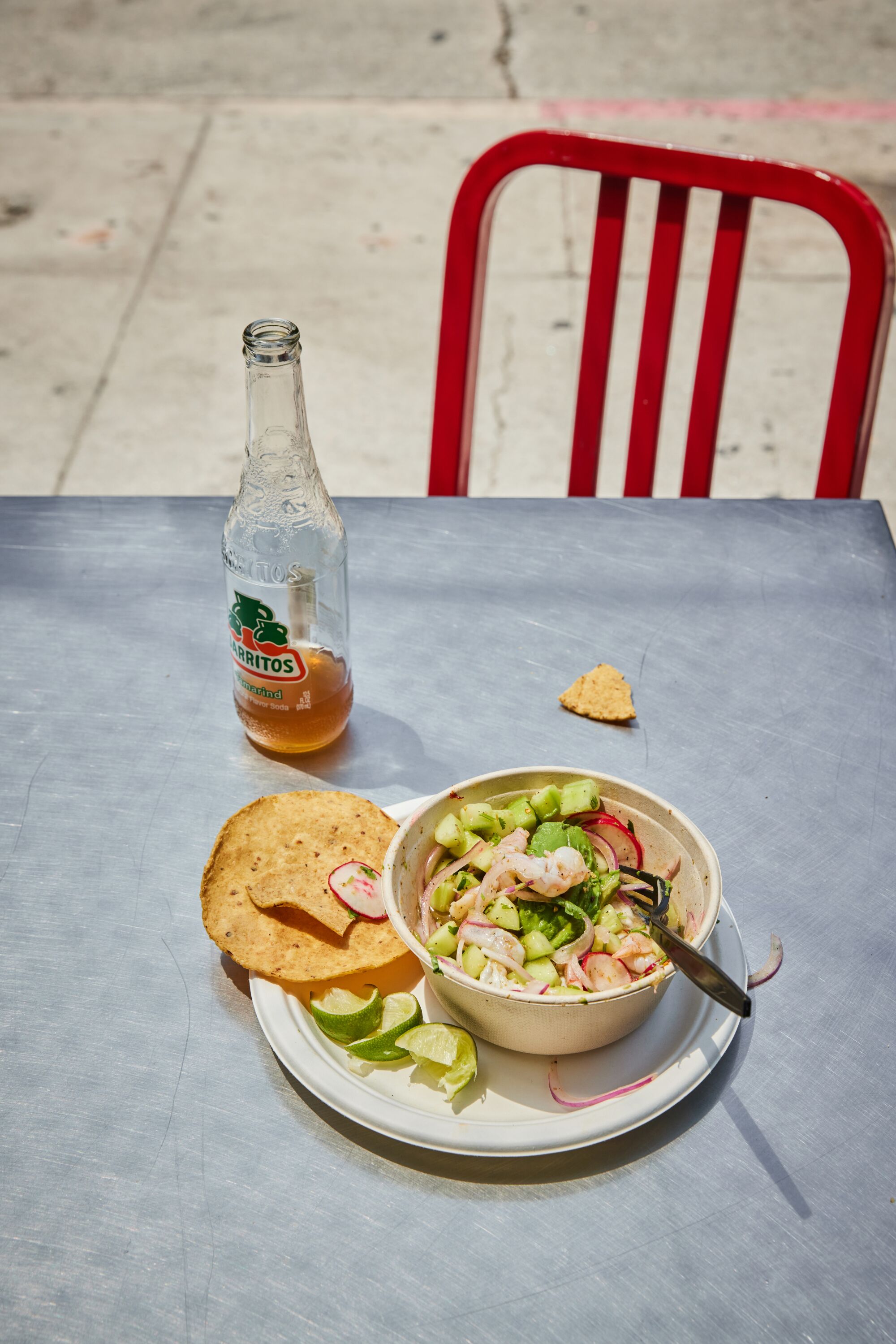 A plate of food and Jarritos bottle sit on a silver table outdoors.