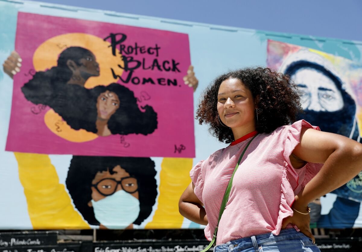 Artist Alexandra Allie Belisle stands before a mural she helped paint that reads "Protect Black Women."