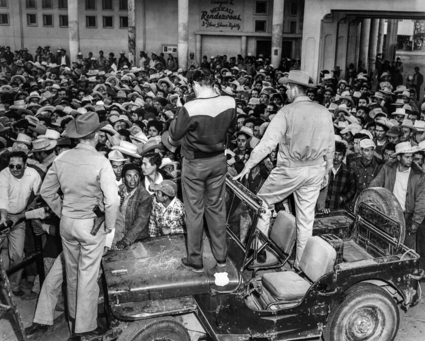 A man stands on a vehicle in front of a crowd of men
