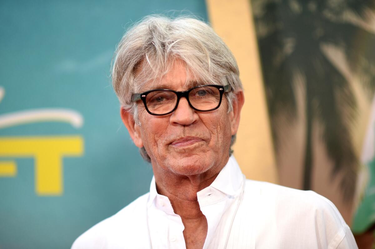 Eric Roberts, in a white collared shirt and black frame glasses, looks into the camera. 