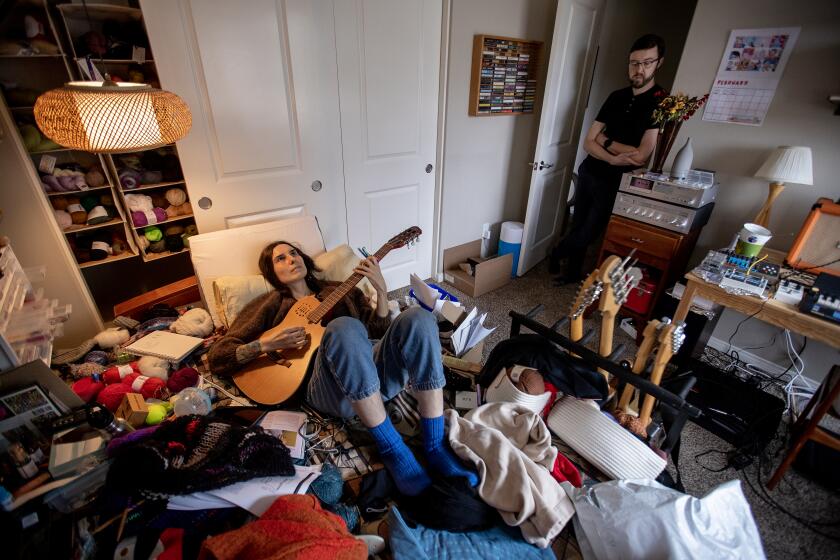 Irvine, CA - February 14: Courtney Gavin, who got sick with Covid in March 2020 and is now sick with long covid, plays guitar in her room, where she spend most of her time. She used to play in a couple bands but is on hold until she recovers at her home with her husband, Connor Mayer. Photo taken Tuesday, Feb. 14, 2023 in Irvine, CA. (Allen J. Schaben / Los Angeles Times) Courtney is experiencing long covid and the costs (emotionally, physically and financially) this disease has had on their lives. She currently is not working and has severe shortness of breath, needs help doing basic tasks in the home (pushed in a wheelchair, uses a chairlift) and is fatigued easily. Connor works as a professor at UC Irvine and is now her full-time caregiver. He noted he is struggling with balancing the responsibilities of being a caregiver over his career responsibilities (which has resulted in a loss of income).The couple has shared that they have spent over $60k in medical expenses (chair lift, wheelchair, supplements), Courtney plays music and is largely bedridden, but they seem to have a routine where Connor makes her food and sets up everything before he leaves for work to make it as easy as possible for her to eat and take care of herself. Courtney also applied for disability and was denied recently.