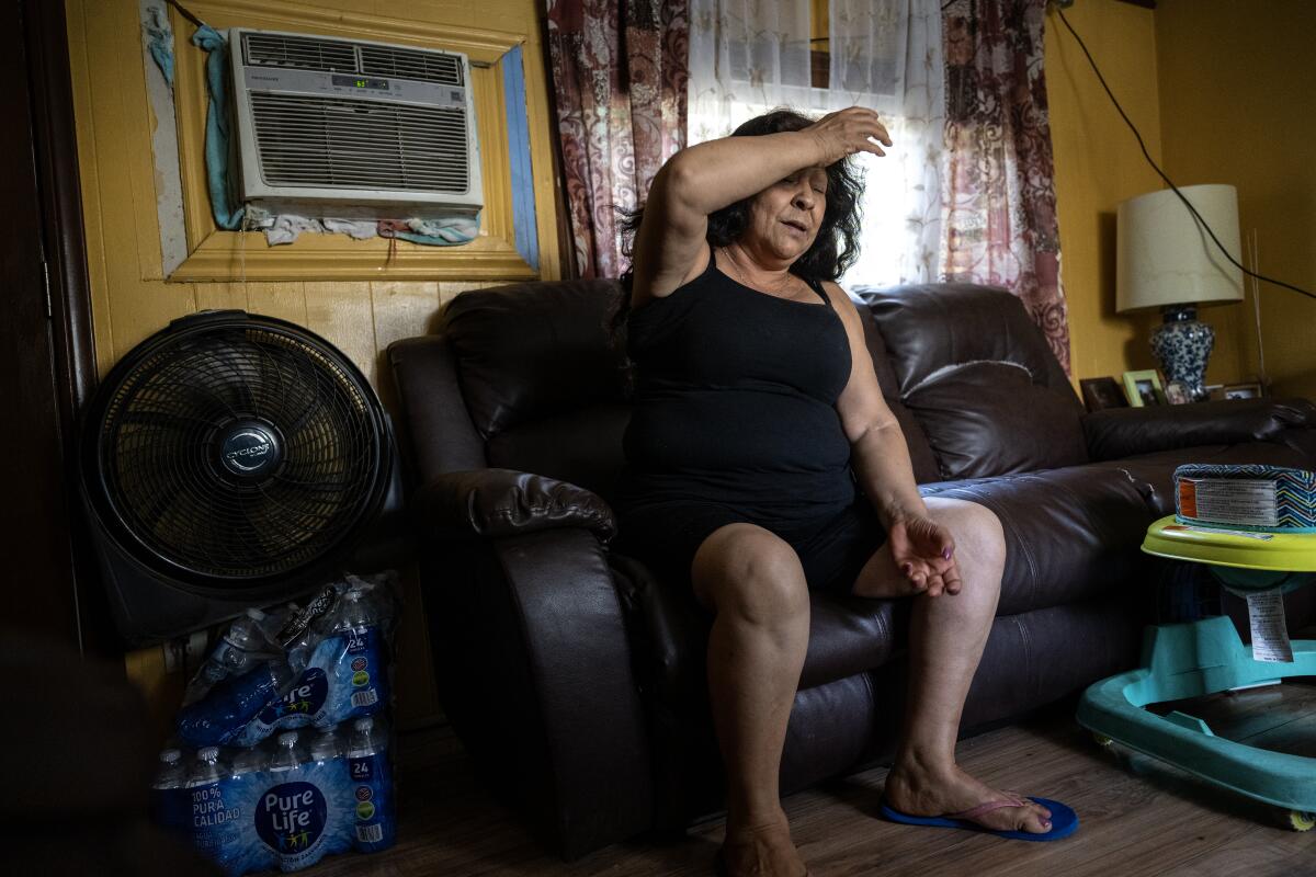 A woman sits on a couch in her mobile home during high temperatures