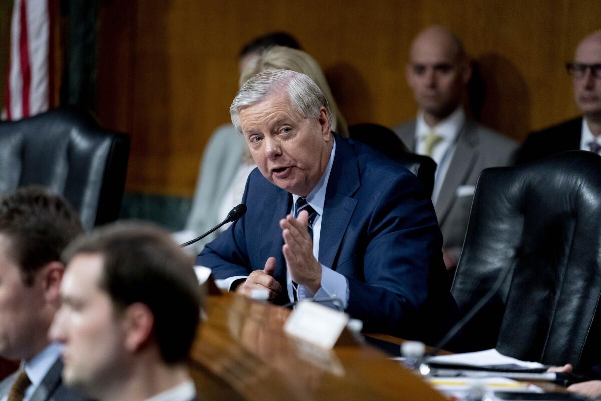 Sen. Lindsey Graham sits among other people in a wood-paneled room and talks.