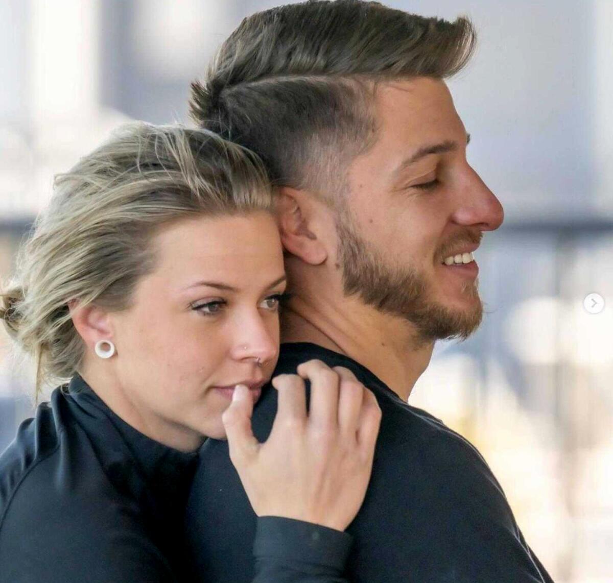 A woman rests her head behind the head of a man, both dressed in black shirts.