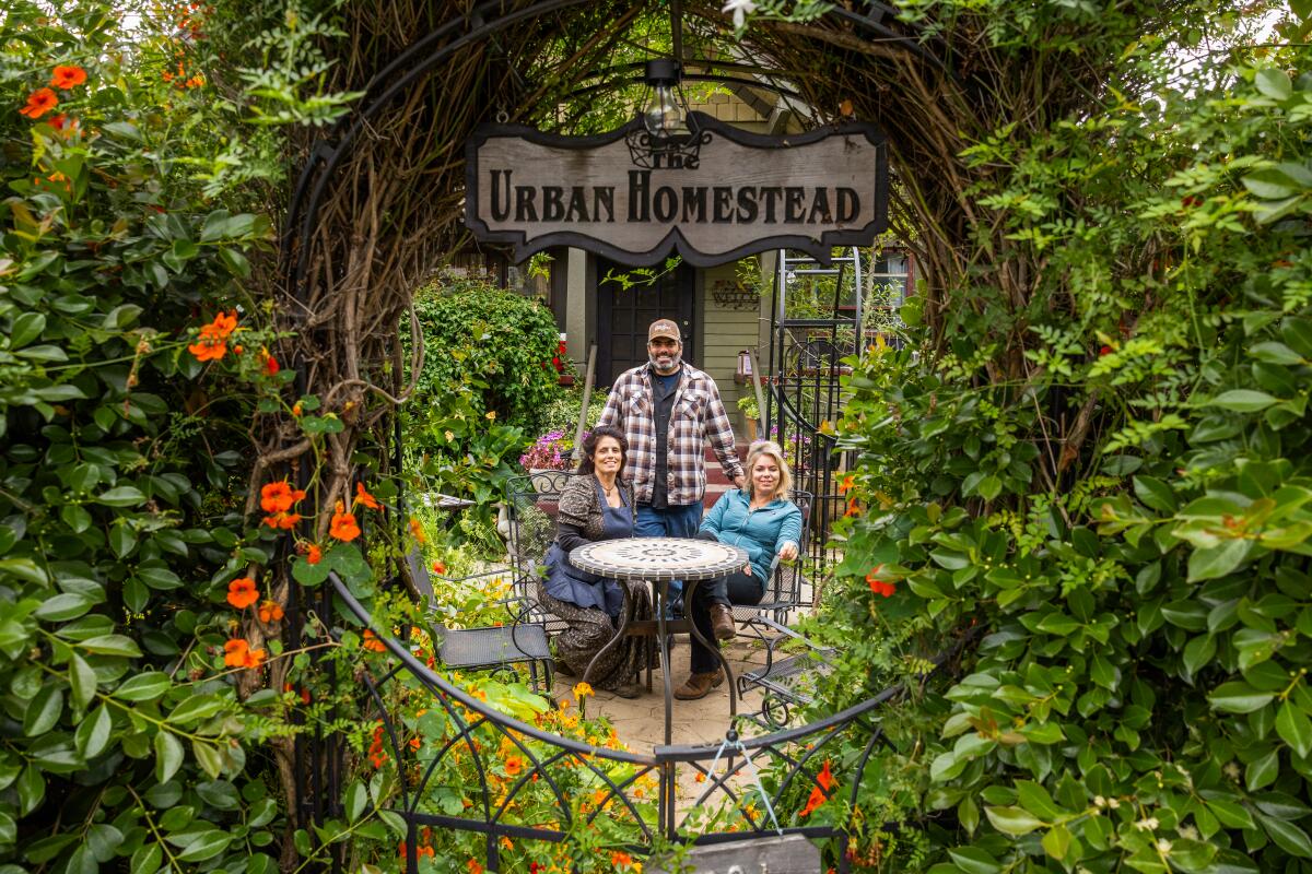 Two women sitting and a man standing are seen through an opening under a sign reading "The Urban Homestead" in Pasadena.