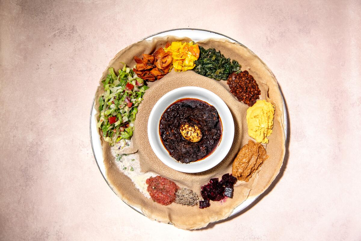 A round plate covered with brown flat bread with dollops of vegetables and a dish of doro wat in the center