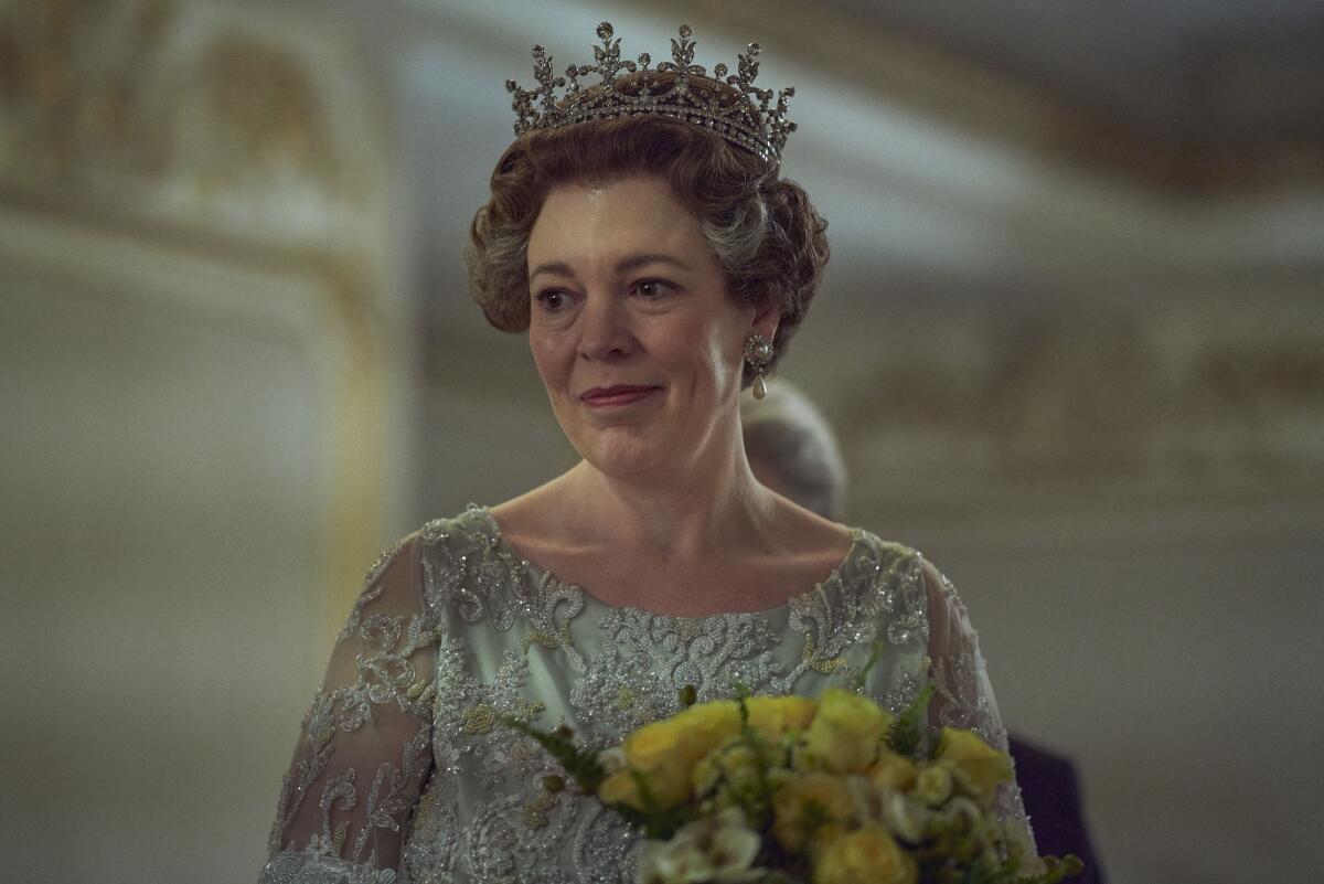 Olivia Colman dressed as Queen Elizabeth II in a bejeweled crown holding yellow flowers