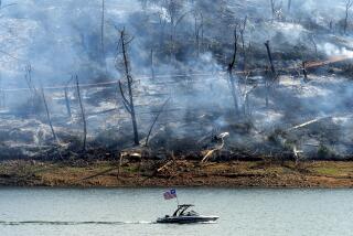 A boat crosses Lake Oroville with a smoldering hillside behind as the Thompson Fire burns in Oroville, Calif., on Wednesday, July 3, 2024. An extended heatwave blanketing Northern California has resulted in red flag fire warnings and power shutoffs. (AP Photo/Noah Berger)