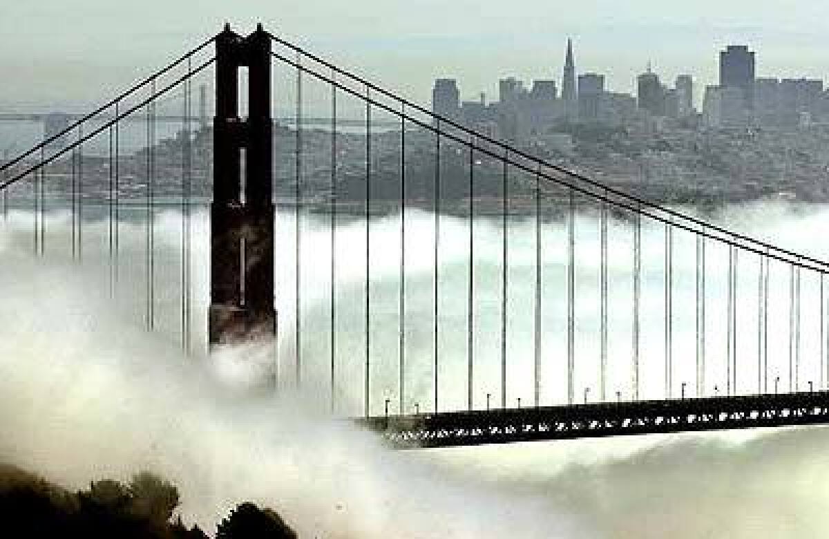 The outline of the San Francisco skyline is seen beyond the fog-shrouded Golden Gate Bridge.