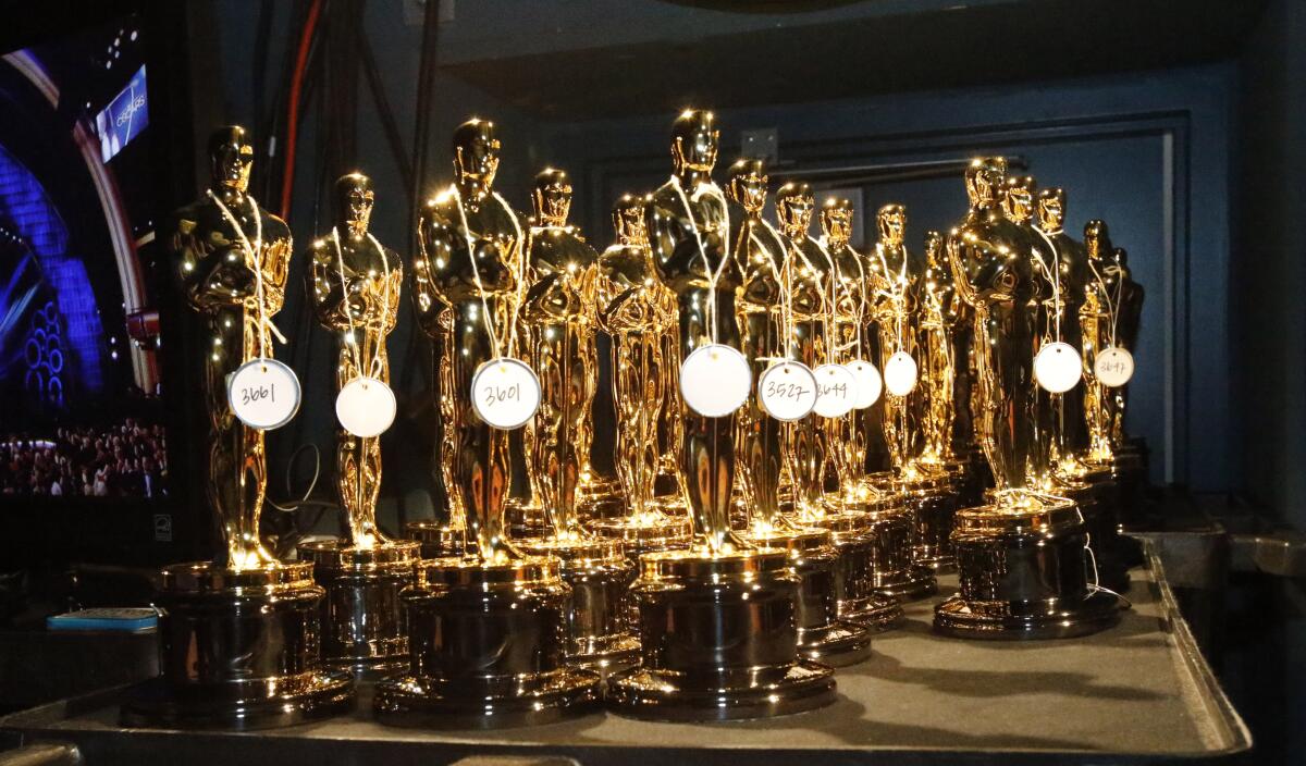 A bunch of Oscar statuettes with tags on them are grouped on a table.