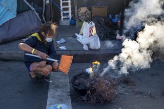 Los Angeles, CA - December 09: Toxic smoke billows up over a line of tents on the sidewalk as a person burns the plastic off copper wires in skidrow on Friday, Dec. 9, 2022, in Los Angeles, CA. They were using a broom the fan the flames. (Francine Orr / Los Angeles Times)