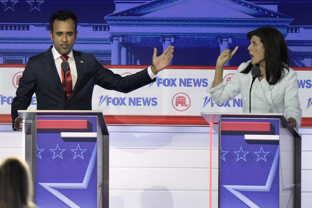 A man in a dark suit and a woman in a white suit speak during a Republican presidential primary debate