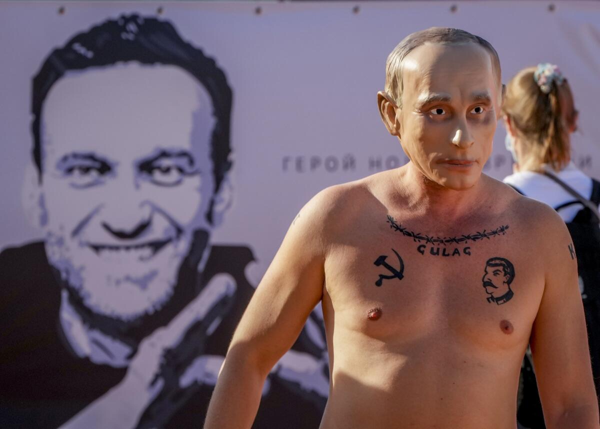 A man wearing a Vladimir Putin mask takes part in a demonstration for imprisoned Alexei Navalny, poster at left, in Geneva, Switzerland Tuesday, June 15, 2021. US President Joe Biden and Russia President Vladimir Putin will meet for talks in Geneva on Wednesday. (AP Photo/Michael Probst)